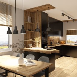 Mudi Agnieszka Kasprzyk - Nowoczesna kuchnia z drewnianymi akcentami: czarne szafki, drewniany blat i stół z szarymi krzesłami. Duże okno z widokiem na jesienny krajobraz.