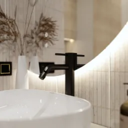 Nowoczesna łazienka z owalną umywalką, czarną armaturą i podświetlanym lustrem. Beżowe płytki imitujące kamień i dekoracyjne trawy pampasowe dodają elegancji.