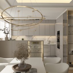 Mudi Agnieszka Kasprzyk - Elegancka, jasna kuchnia z jadalnią. Białe meble, marmurowy backsplash, złoty żyrandol i przeszklona witryna. Minimalistyczny wystrój z akcentami roślinnymi.