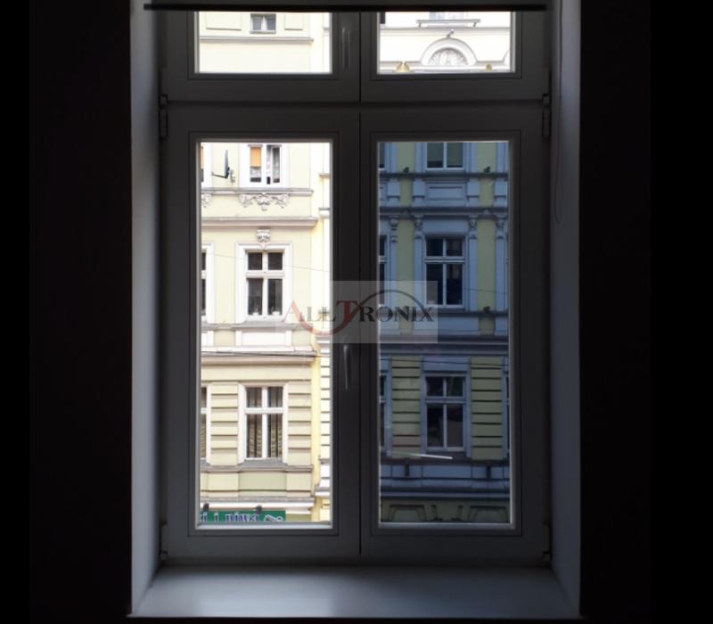 Widok z okna na kamienice po drugiej stronie ulicy, okno z widocznym logo firmy na szybie.