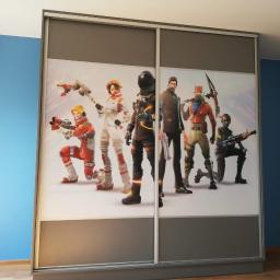 Awan Meble - Szafa przesuwna z motywem Fortnite, szare ramy, białe fronty z postaciami z gry, na tle niebieskiej ściany.