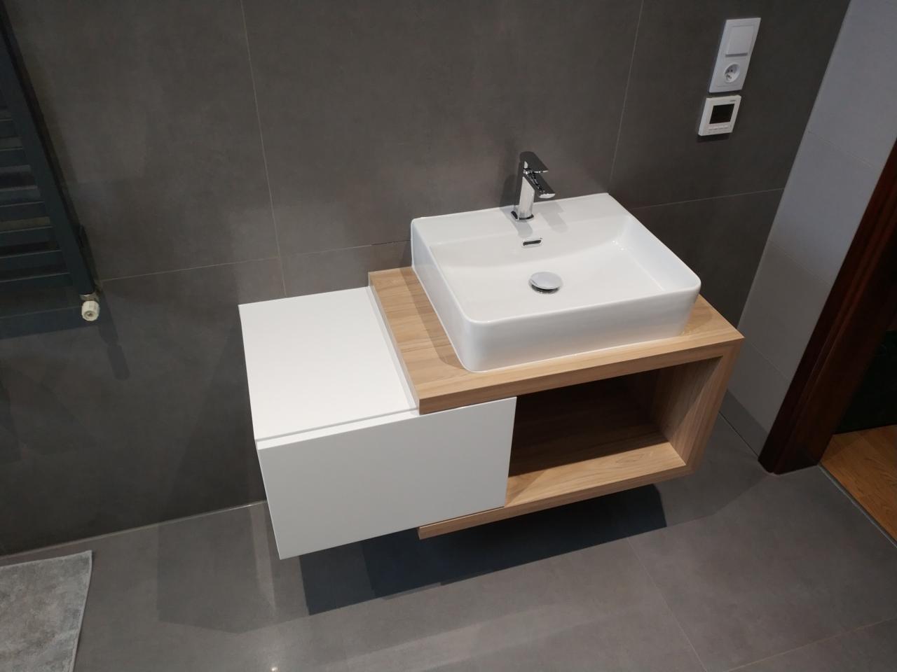 Nowoczesna łazienka z wiszącą szafką pod umywalkę, biały front szuflady, blat z jasnego drewna, prostokątna umywalka nablatowa i chromowana bateria.