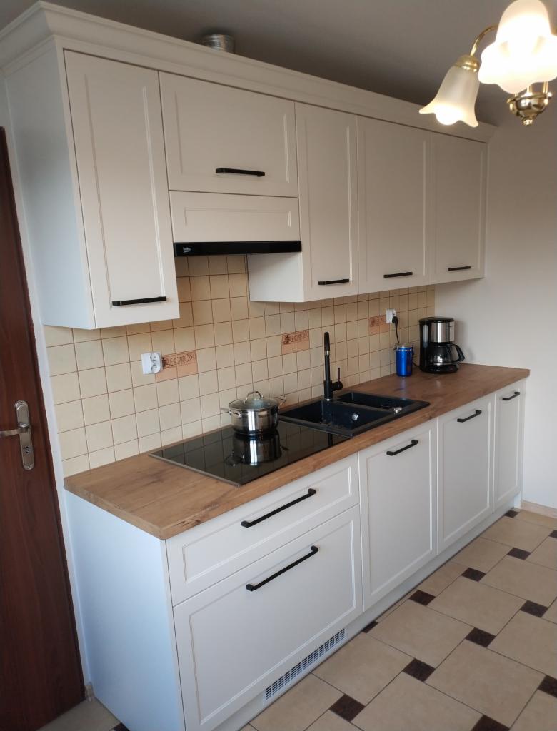 Jasna kuchnia z drewnianym blatem w Działoszynie, z czarnymi uchwytami i płytą indukcyjną z garnkiem.