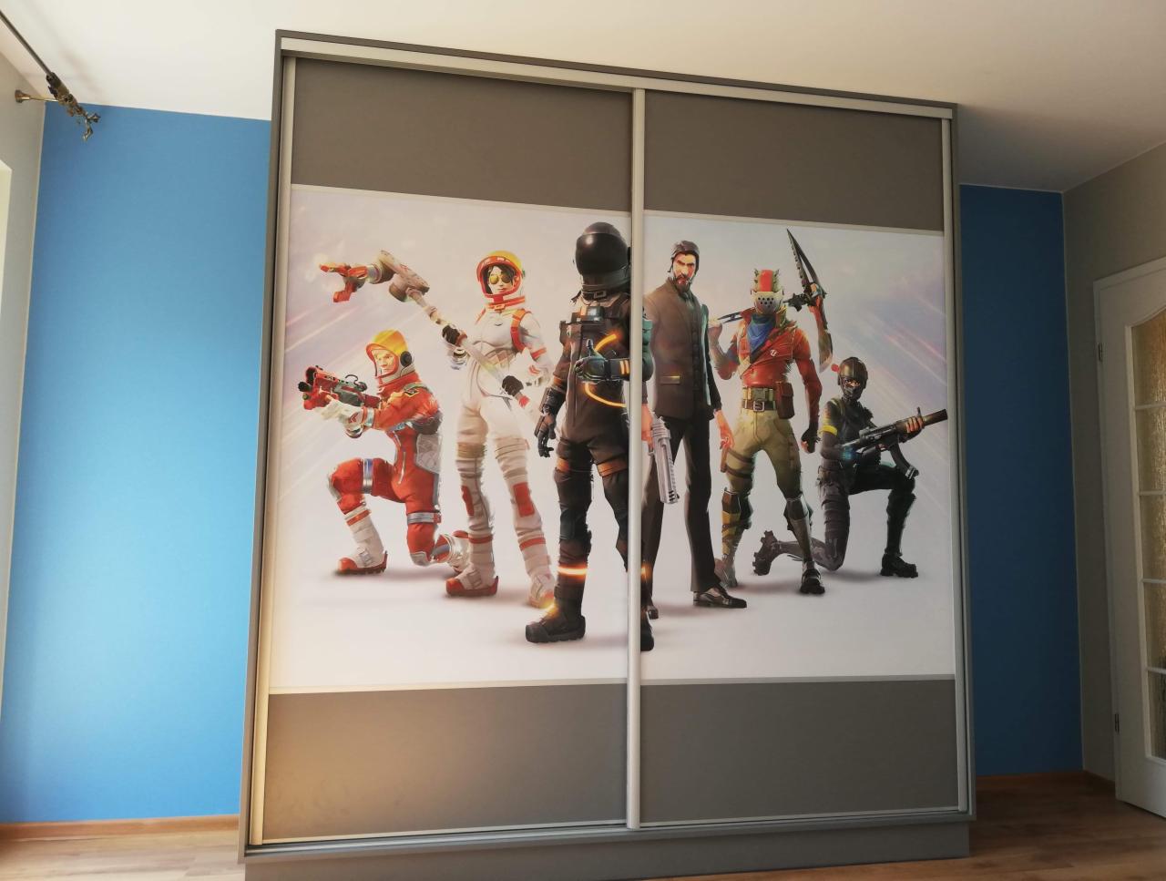 Szafa przesuwna z motywem Fortnite, szare ramy, białe fronty z postaciami z gry, na tle niebieskiej ściany.
