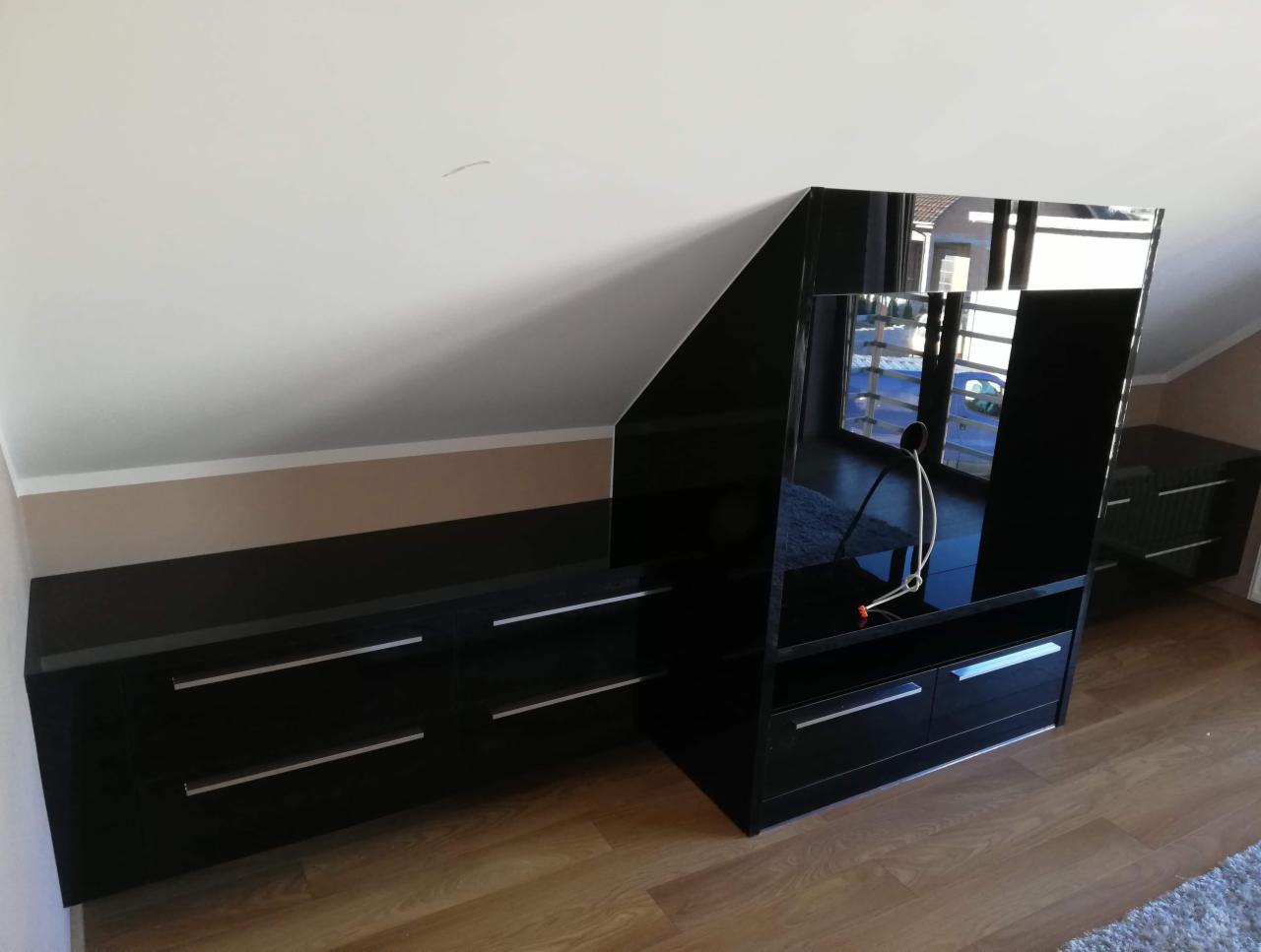 Czarna, lakierowana zabudowa pod skosem na poddaszu, z szafkami i regałem, widoczne odbicie okna.