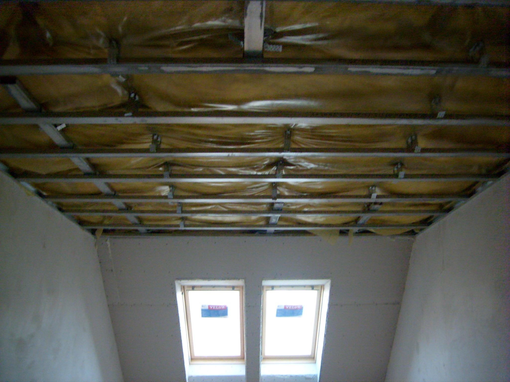 Montaż sufitu podwieszanego z izolacją i ścianek działowych w pomieszczeniu z dwoma oknami dachowymi.