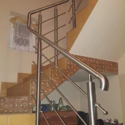 Dominik Starzyński - Schody z żółtymi płytkami i balustradą ze stali nierdzewnej, widok z dołu, w tle szafka i półka na buty.