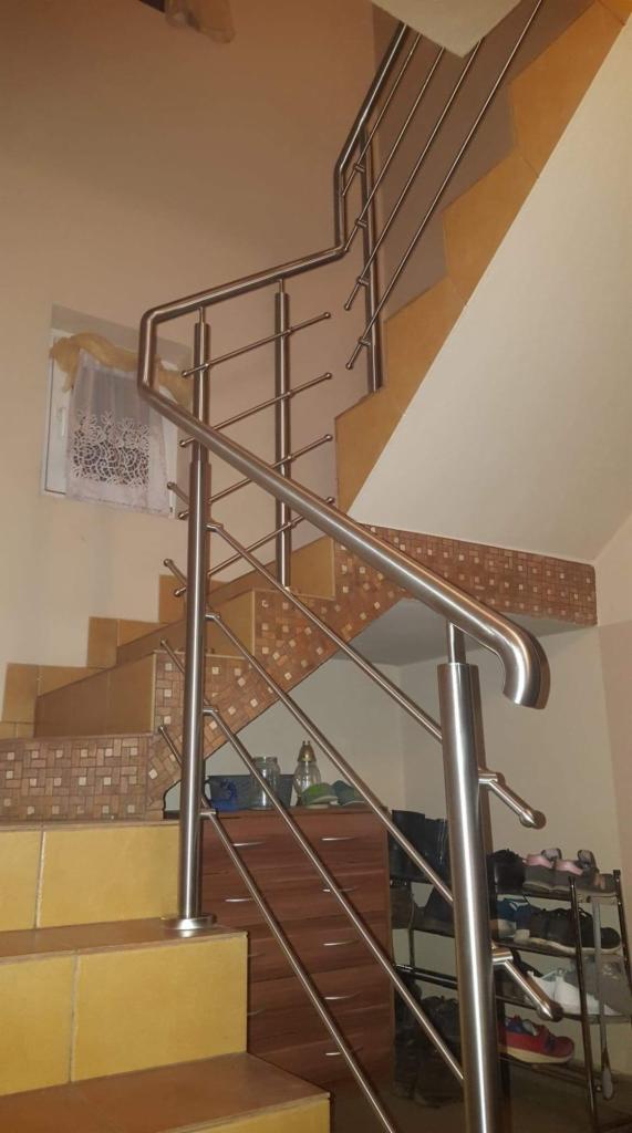 Schody z żółtymi płytkami i balustradą ze stali nierdzewnej, widok z dołu, w tle szafka i półka na buty.