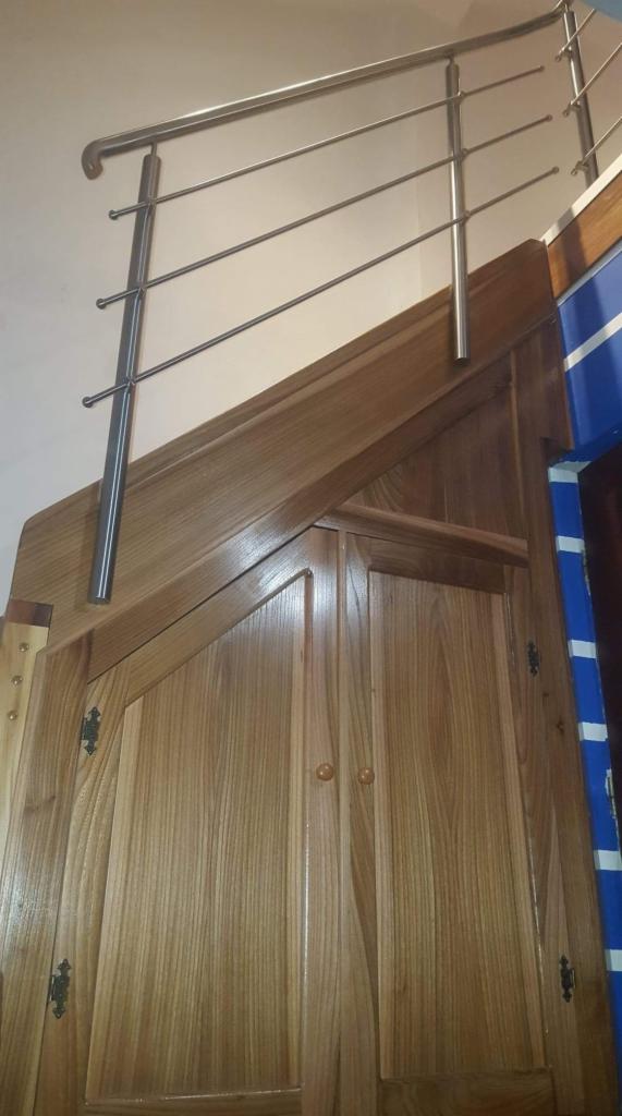 Nierdzewna poręcz schodowa z czterema poprzeczkami zamontowana na drewnianej obudowie schodów z szafkami.