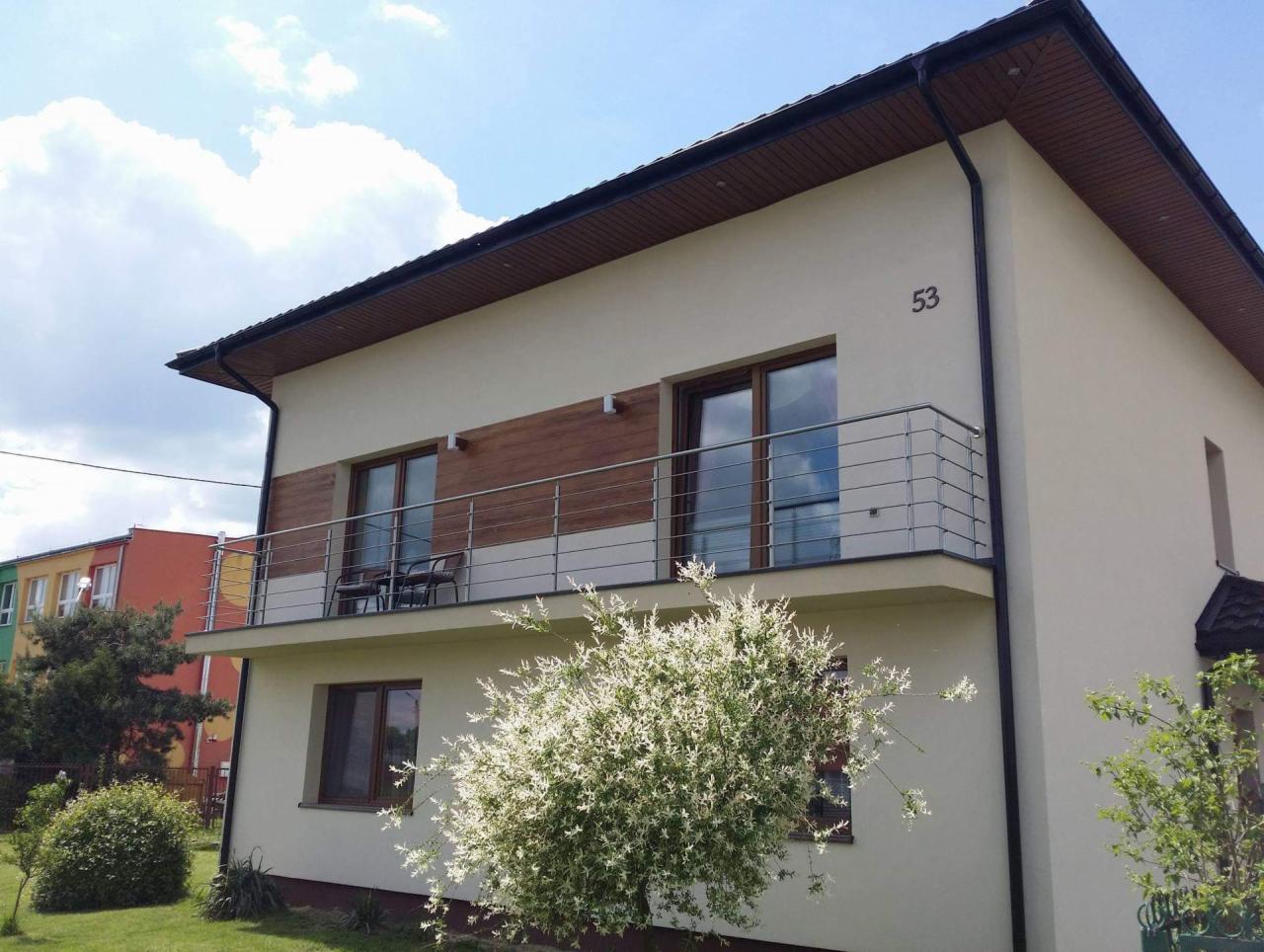Nowoczesny dom z balkonem zabezpieczonym metalową, poziomą balustradą ze stali nierdzewnej, widok z poziomu trawnika, na ścianie numer 53.