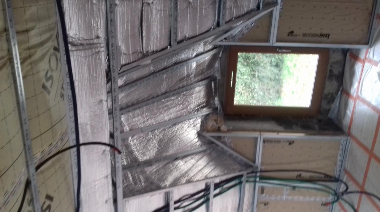 Montaż izolacji z folią aluminiową i stelaża z profili stalowych pod płytę karton-gips w poddaszu ze skośnym dachem i oknem.