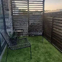 Zaciszny taras na dachu z drewnianą przesłoną, sztuczną trawą i minimalistycznymi krzesłami z metalowej siatki.