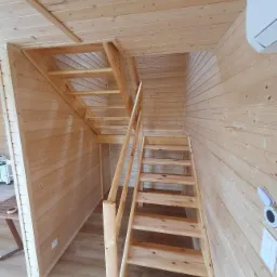 Wnętrze domu z drewnianą boazerią i schodami na poddasze, widoczne elementy wykończeniowe i klimatyzacja.