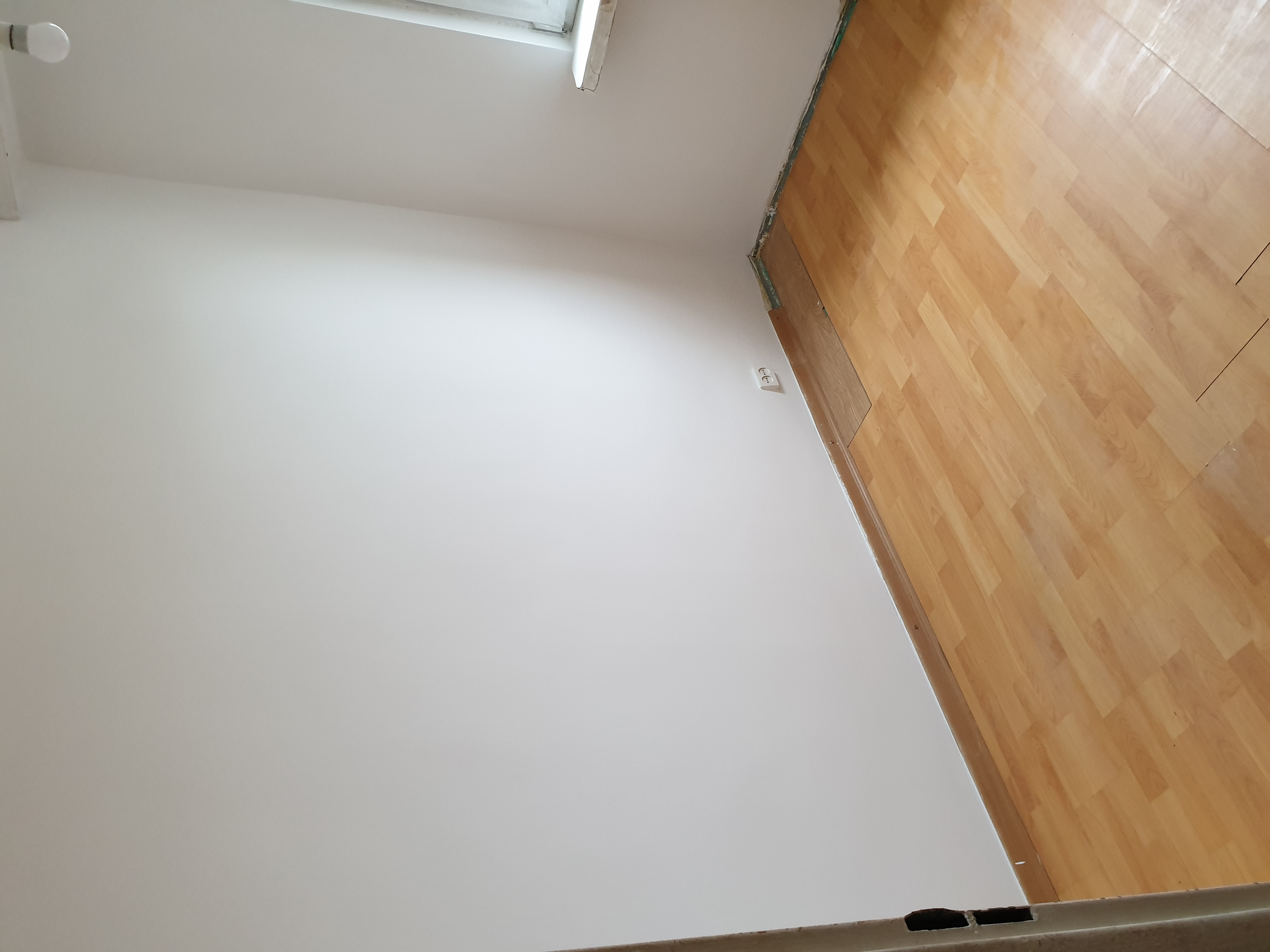 Pokój po malowaniu ścian na biało i ułożeniu paneli podłogowych z widocznym gniazdkiem elektrycznym na ścianie