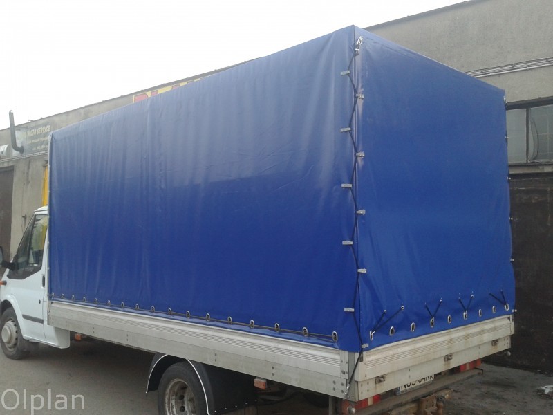 Biały samochód dostawczy z nową, niebieską plandeką, zabezpieczoną mocowaniami na krawędziach.