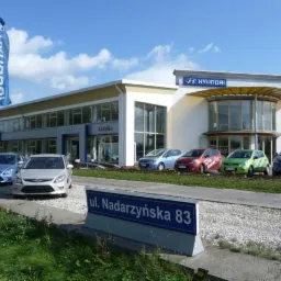 Salon samochodowy Hyundai 'Sobański' z wystawą nowych aut w różnych kolorach na zewnątrz, widoczny znak firmowy na budynku i flaga.
