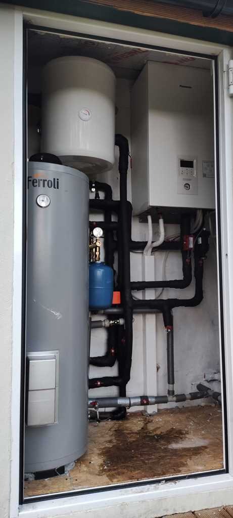 Zestaw urządzeń Ferroli w pomieszczeniu technicznym: zbiornik buforowy, zasobnik ciepłej wody i inne elementy instalacji grzewczej z licznymi rurami.