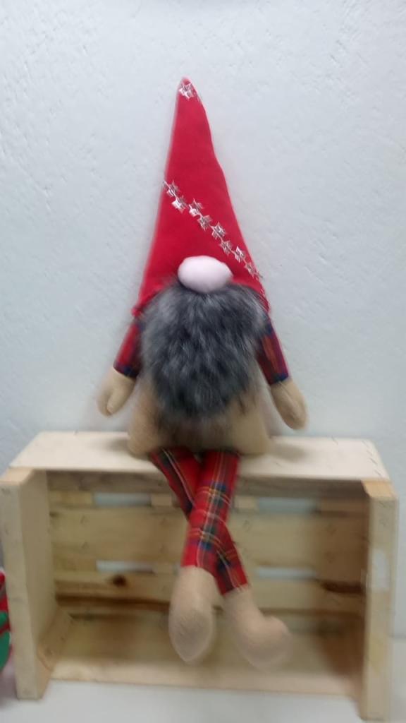 Dekoracyjny, ręcznie szyty skrzat w czerwonym, brokatem zdobionym kapeluszu i spodniach w szkocką kratę, siedzący na drewnianej skrzynce.