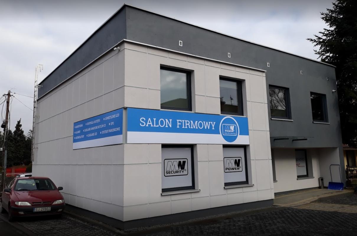 Budynek firmy z szyldem 'Salon Firmowy', oferującej monitoring, kontrolę dostępu, alarmy, oświetlenie LED i systemy parkingowe, z logo 'MW Security' i 'MW Power' w oknach.