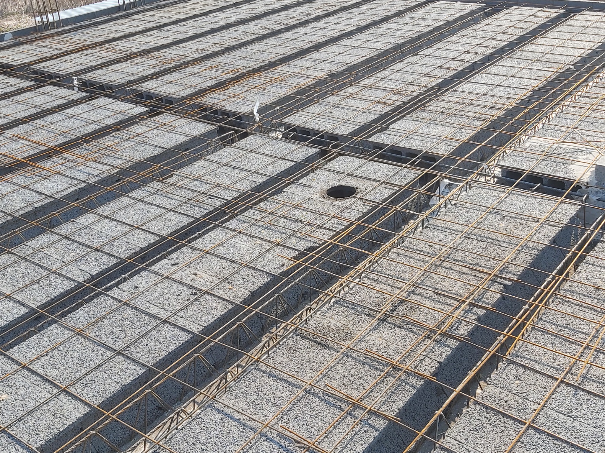 Szare bloczki stropowe zbrojone siatką stalową, widok z góry na budowie, otwór instalacyjny widoczny w jednym z bloczków.