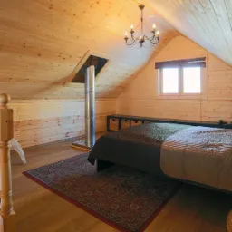 Drewniany pokój na poddaszu z ukośnym sufitem, kominem, łóżkiem i żyrandolem.