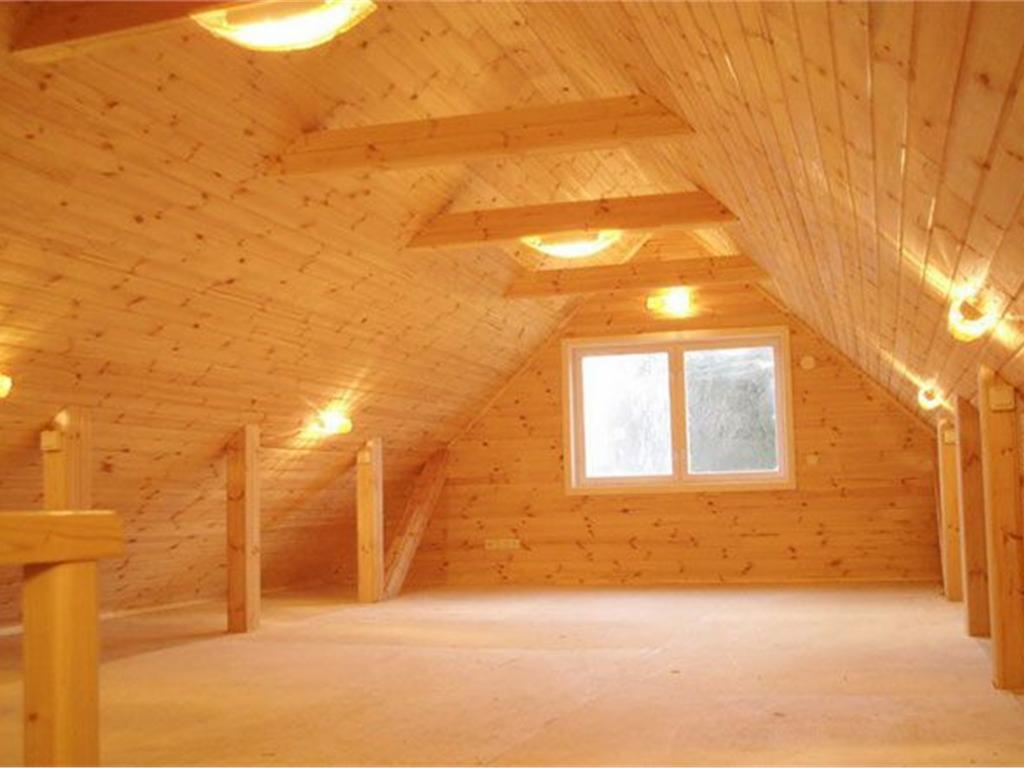 Wnętrze poddasza domu szkieletowego, wykończonego jasnym drewnem, z widocznymi belkami konstrukcyjnymi, oświetleniem punktowym i oknem.