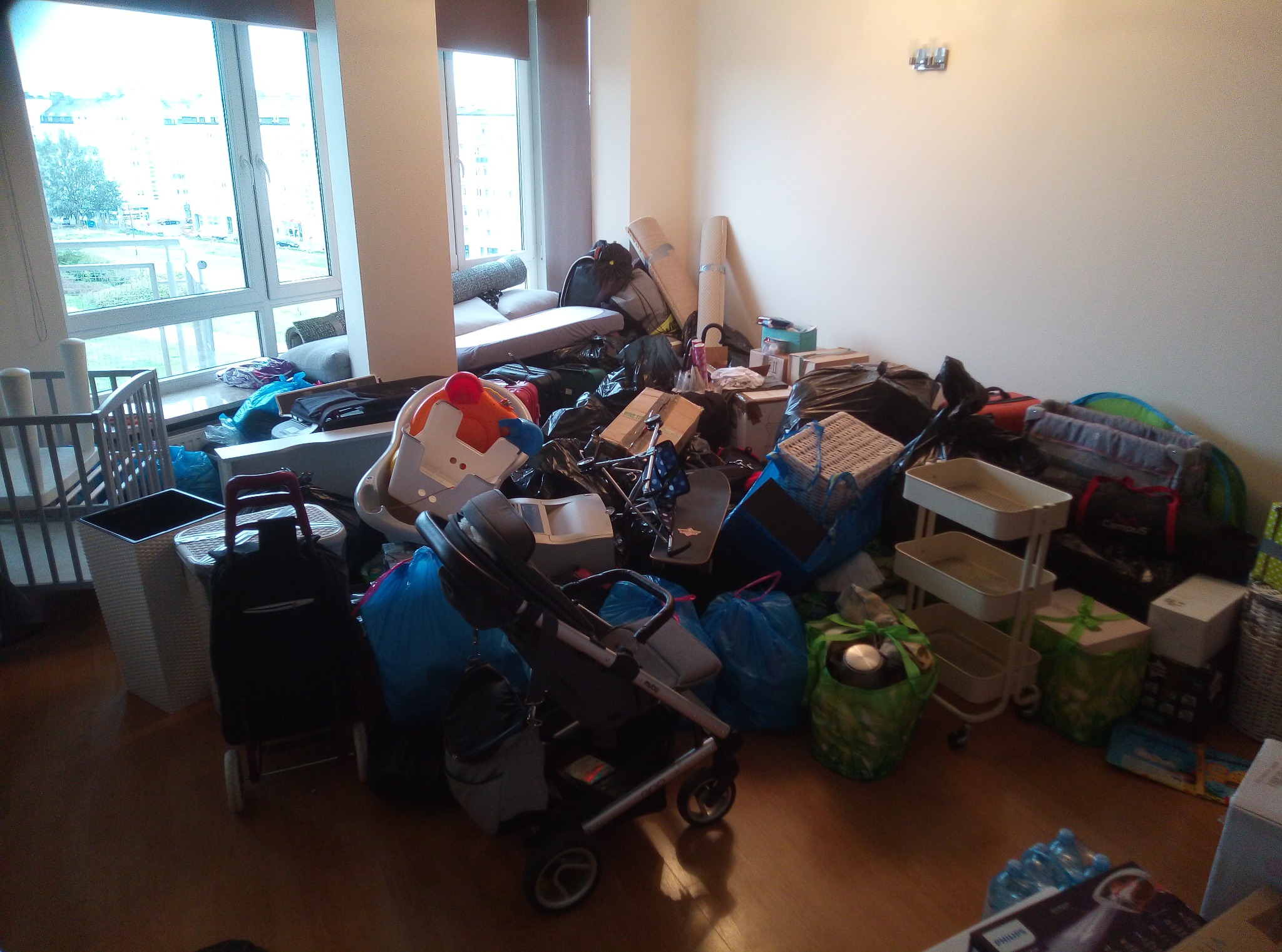 Pokój przed przeprowadzką: nagromadzone przedmioty, w tym wózek dziecięcy, zabawki, torby i meble, czekające na spakowanie.