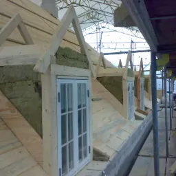 Montaż okien dachowych w konstrukcji drewnianej dachu z izolacją z wełny mineralnej, widok z rusztowania.