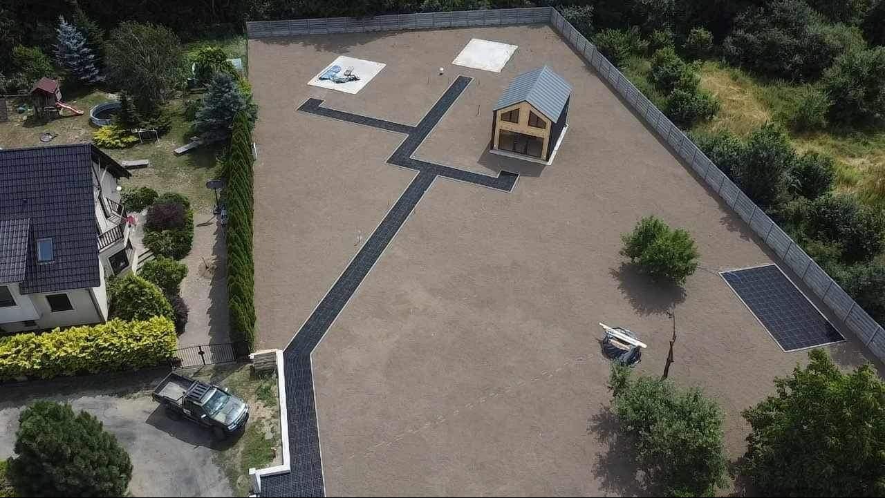 Widok z drona na posesję z nową kostką brukową tworzącą ścieżki, ogrodzeniem panelowym i małym domkiem. Na posesji stoi również budynek mieszkalny i pickup.