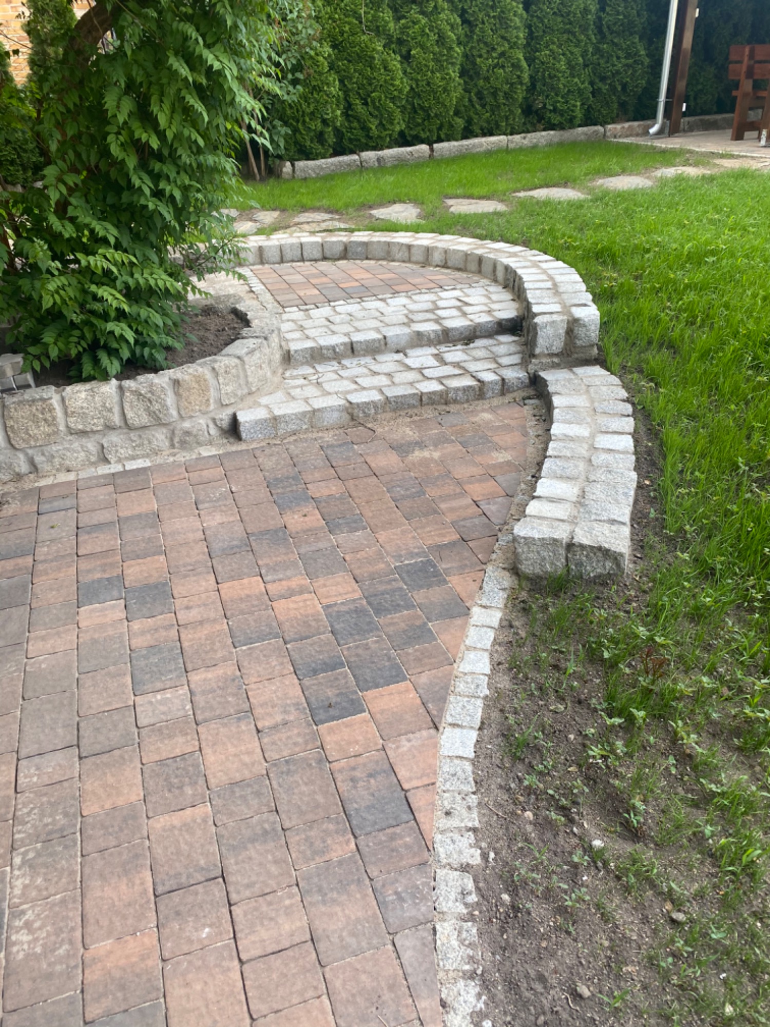 Kaskadowe przejście z kostki granitowej i brukowej, z obrzeżami z kamienia naturalnego, prowadzące przez trawnik z zielenią.