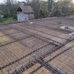 Zbrojenie stropu na deskowaniu z widocznymi dystansami z tworzywa, w tle budynek gospodarczy i drzewa.