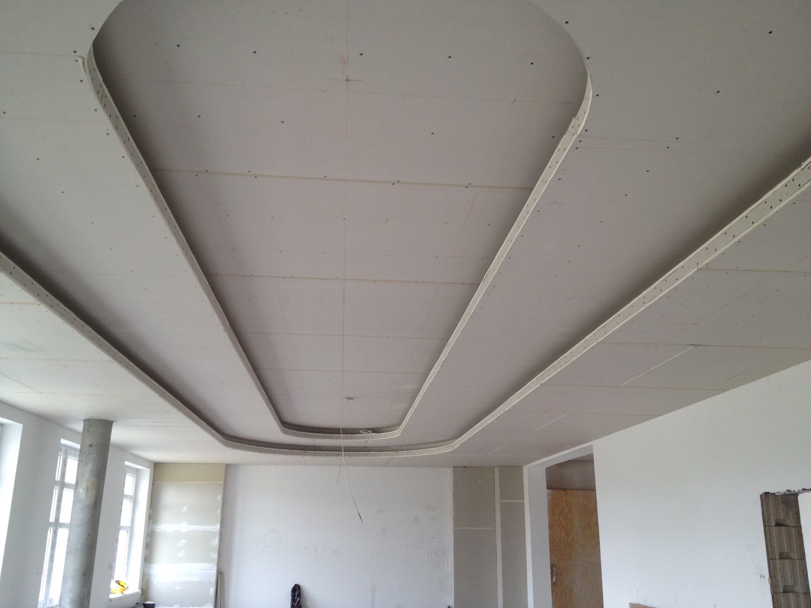 Sufit z elementami dekoracyjnymi wykonanymi z płyt, widoczne profile metalowe i ślady po wkrętach, surowy stan wykończenia, wnętrze w trakcie remontu.