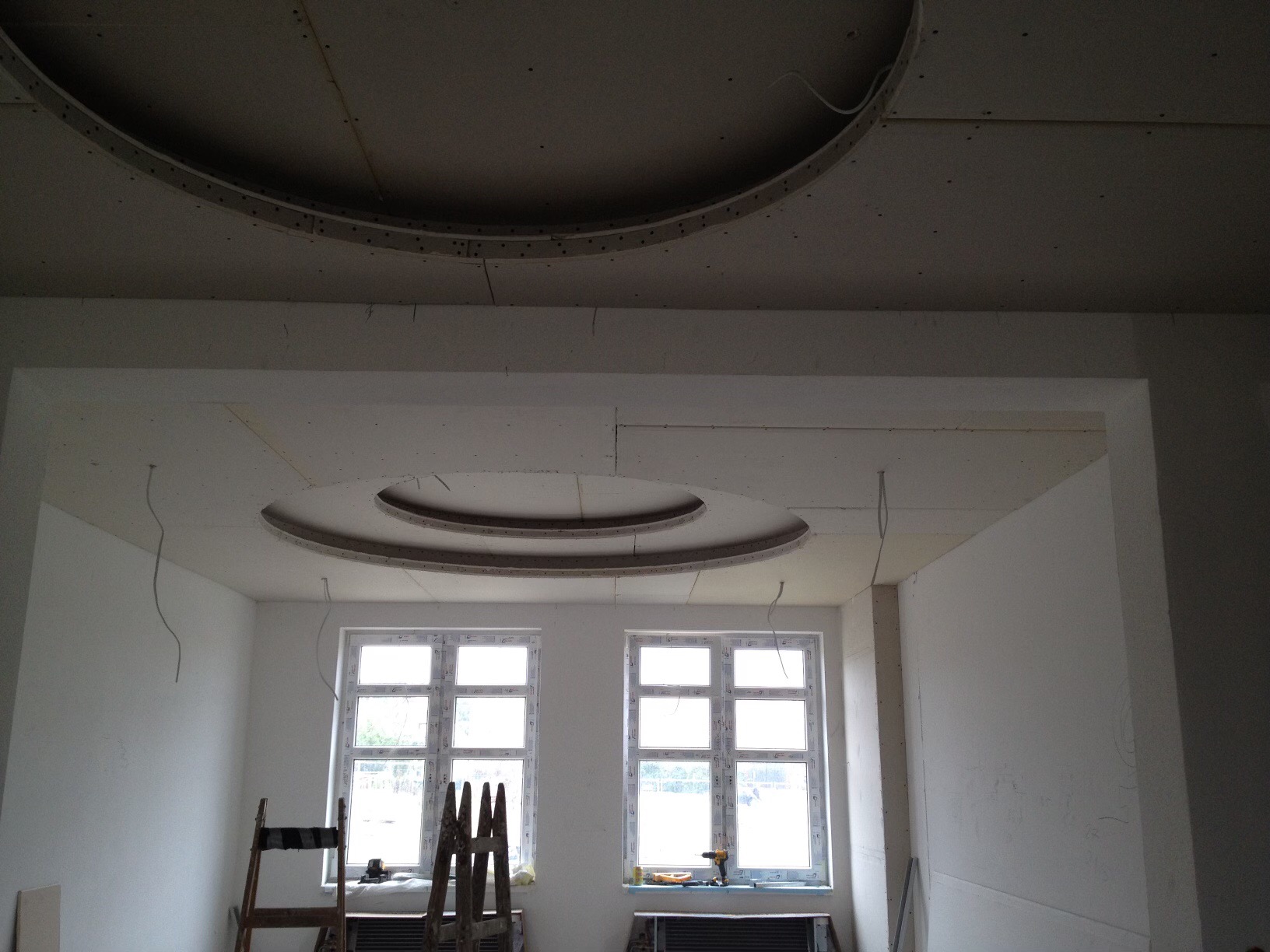 Montaż sufitu podwieszanego z okrągłymi elementami dekoracyjnymi w jasnym wnętrzu, widoczne narzędzia i drabiny.