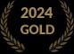 Złoty wieniec laurowy na czarnym tle z napisem '2024 GOLD'. Symbolizuje prestiżowe wyróżnienie lub certyfikat jakości.