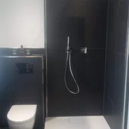 Nowoczesna łazienka z czarnymi płytkami, białą toaletą podwieszaną i brodzikiem bezprogowym, minimalistyczna armatura.