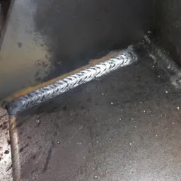 Wewnętrzny narożnik konstrukcji ze stali, z widocznym świeżym spawem o charakterystycznym wzorze jodełki, na powierzchni widoczne ślady po obróbce.