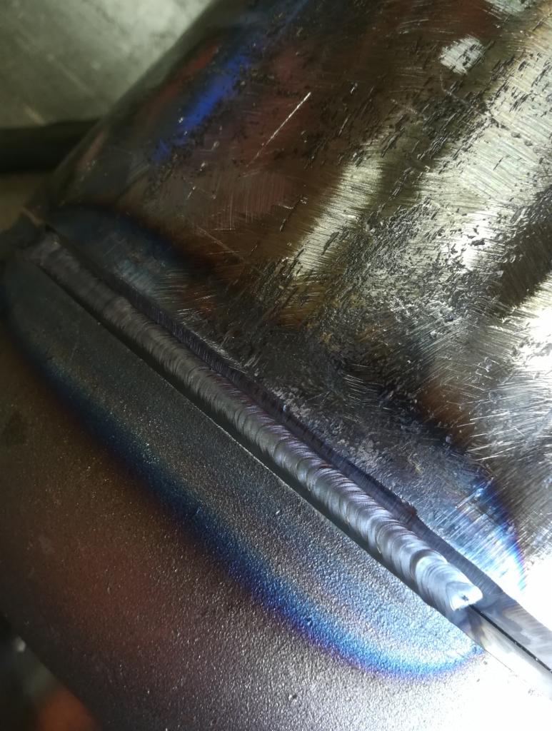 Spoina na metalowej rurze z widocznymi śladami obróbki i tęczowymi przebarwieniami termicznymi.
