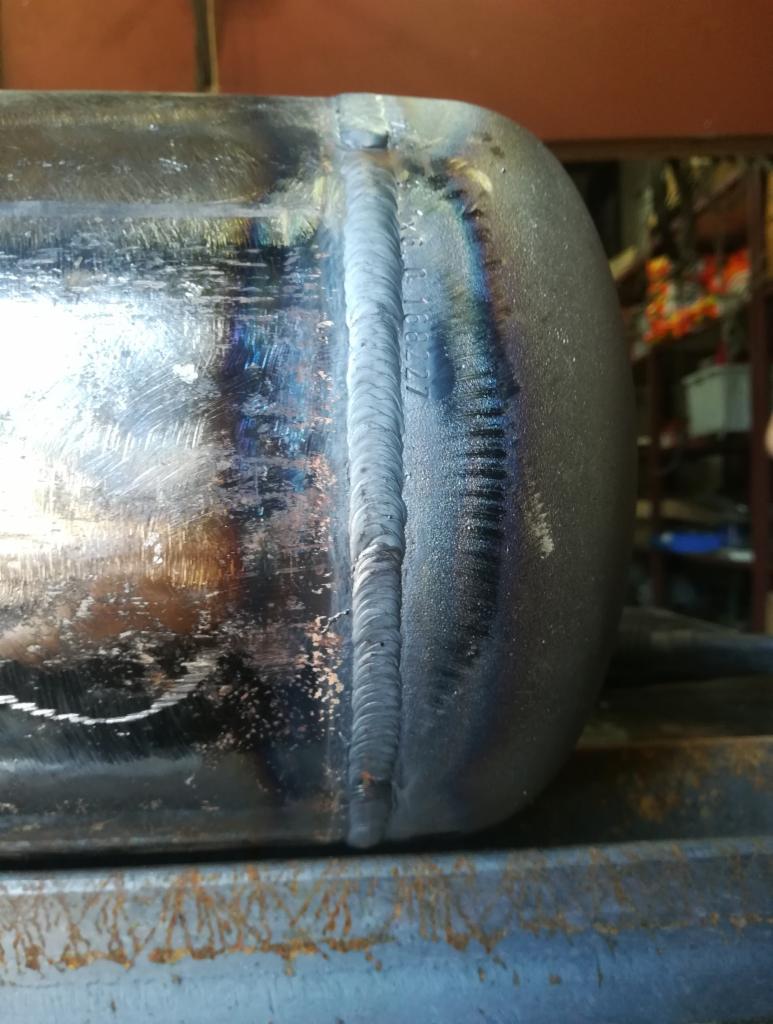 Zbliżenie na spawany zbiornik ciśnieniowy z widocznym szwem spawalniczym i opalizującą powierzchnią metalu.