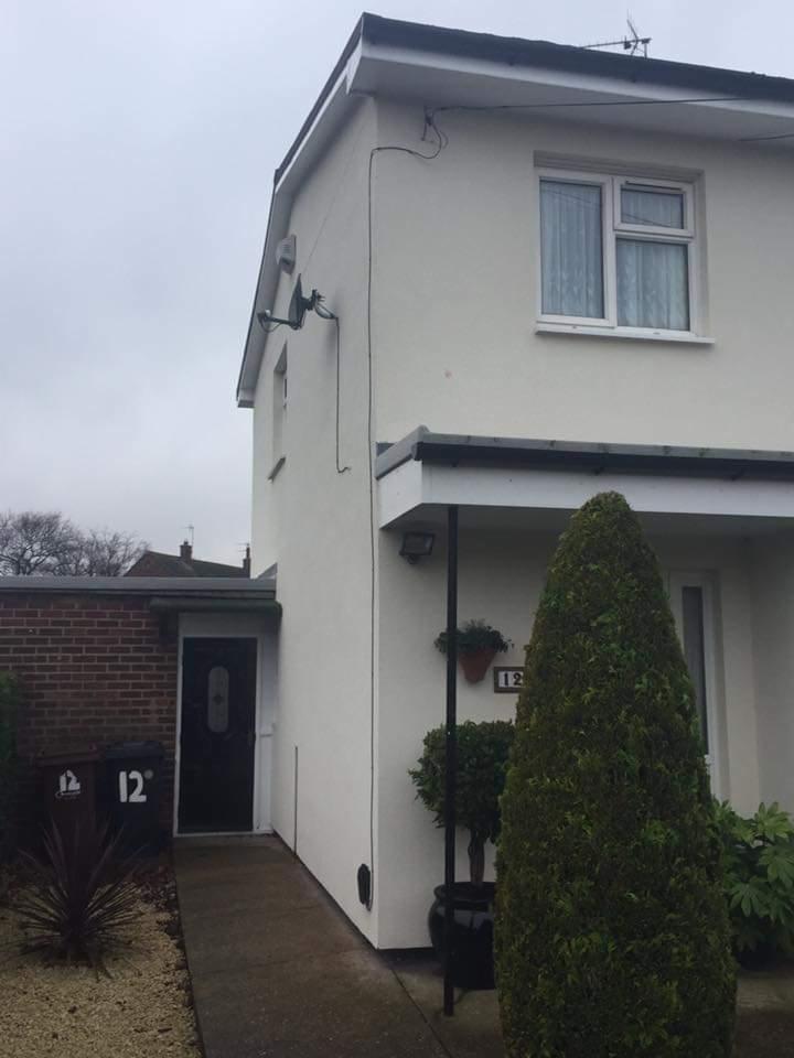 Jasna elewacja domu jednorodzinnego po ociepleniu, widoczne anteny satelitarne i numer domu na śmietnikach.