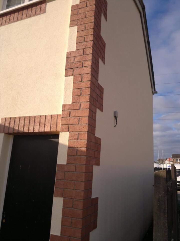 Wykończona elewacja budynku z dekoracyjnym narożnikiem z czerwonej cegły oraz beżowym tynkiem strukturalnym.