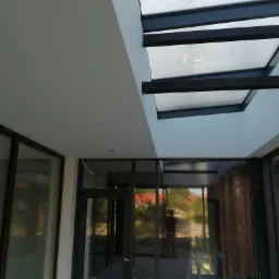 Nowoczesne wnętrze z przeszklonym sufitem i czarnymi ramami, widoczne niedoskonałości na szkle, odzwierciedlające krajobraz na zewnątrz, w trakcie wykańczania.