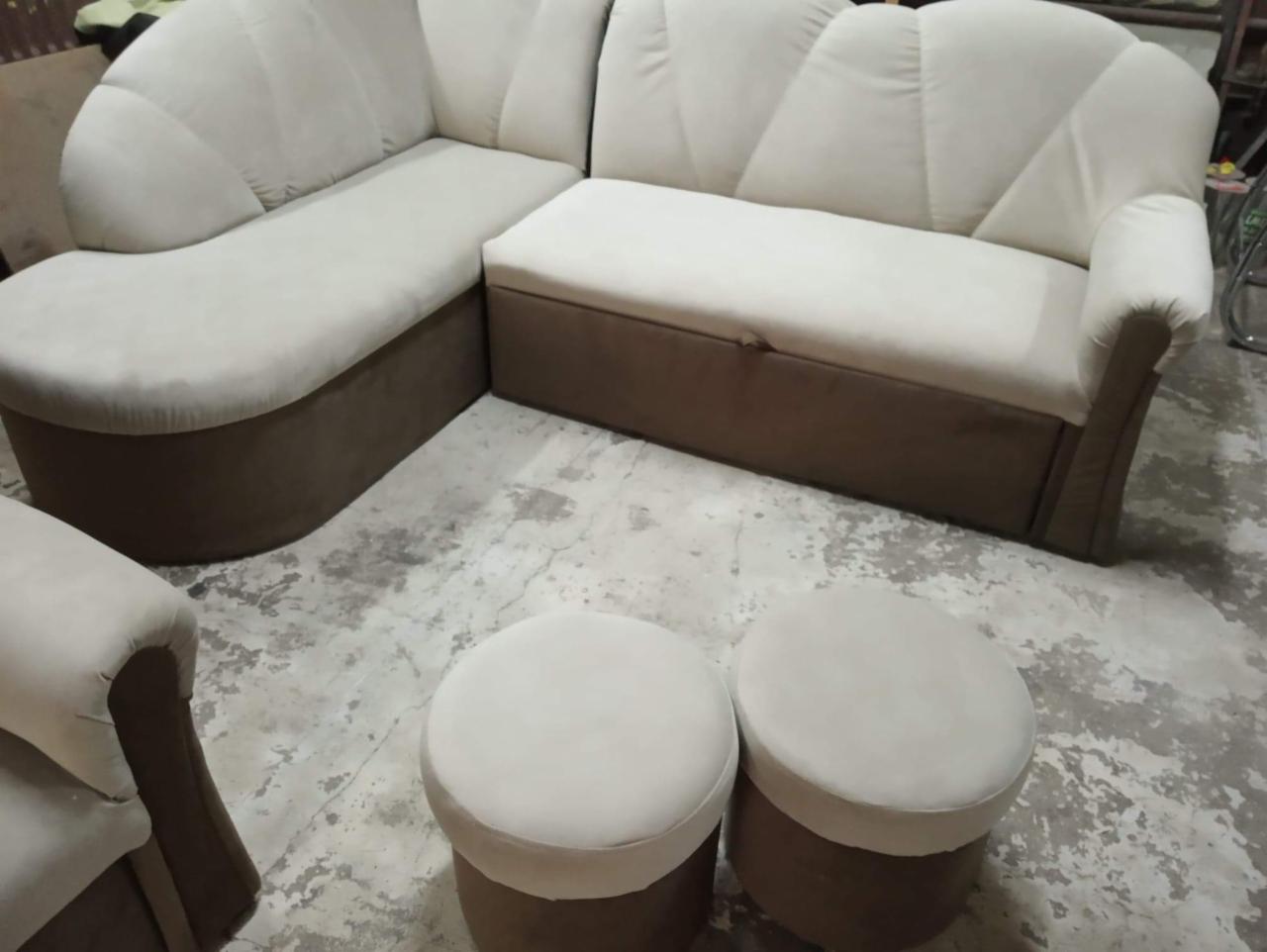 Beżowy narożnik tapicerowany z pufami na betonowej podłodze, widoczne przeszycia na oparciu w kształcie muszli.