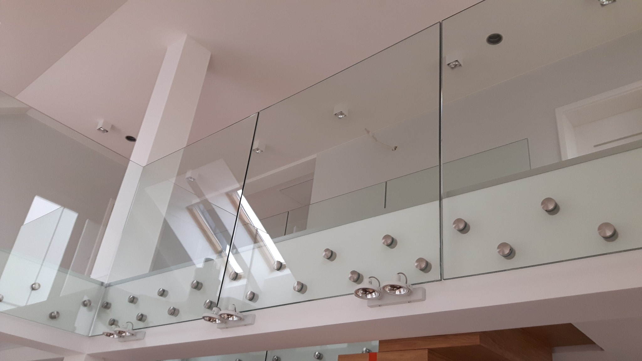 Szklana balustrada wewnętrzna na antresoli, mocowana punktowo, widok z dołu, oświetlenie halogenowe.