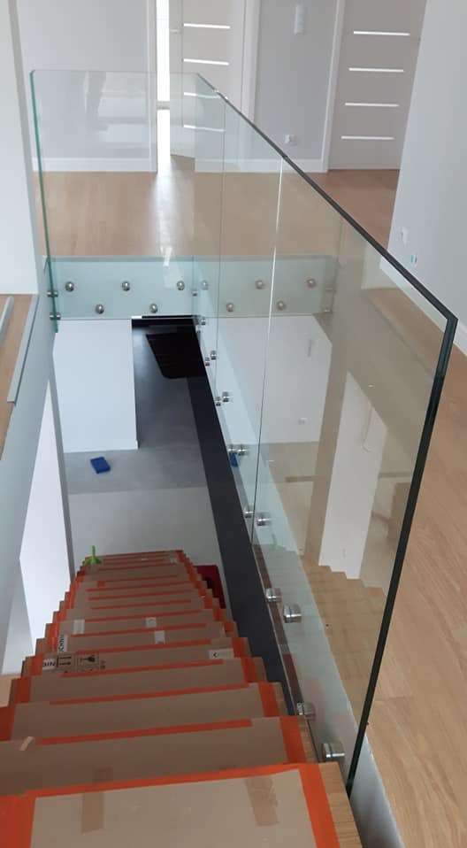 Szklana balustrada z metalowymi mocowaniami zabezpieczająca schody wyłożone kartonem ochronnym podczas remontu, widok z góry.