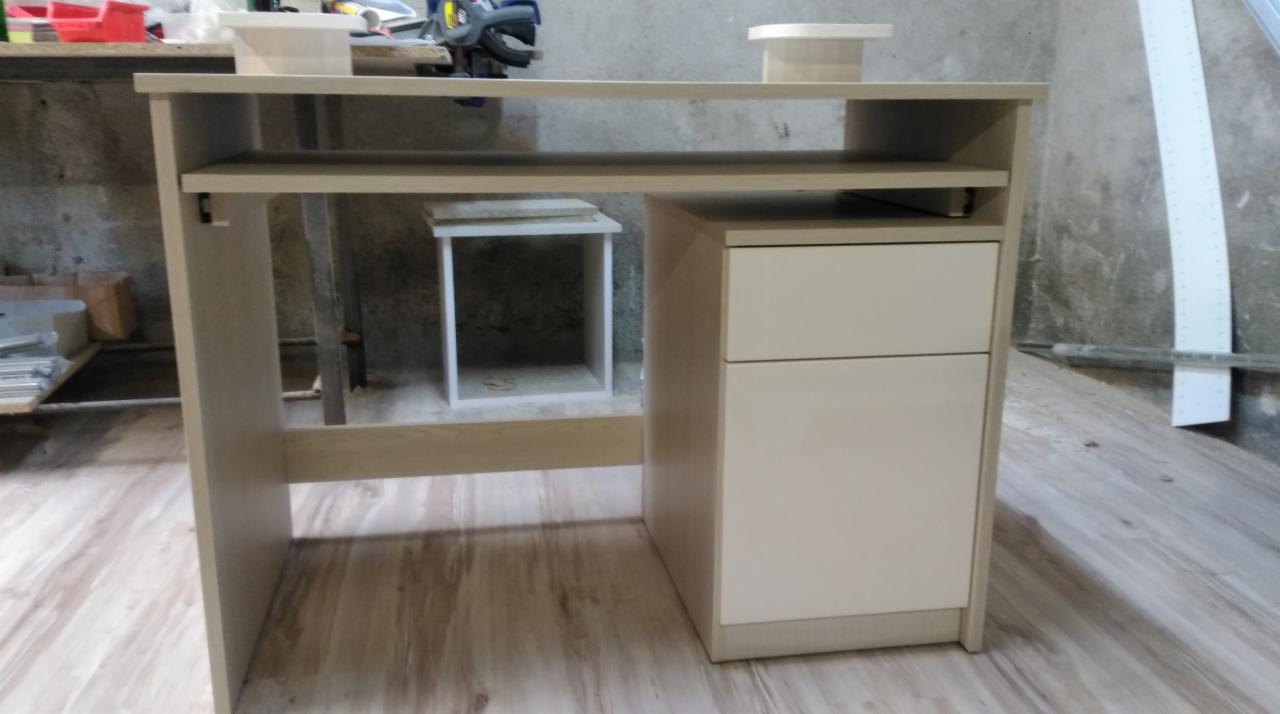 Biurko z jasnego drewna z szufladami i półką, widoczne w warsztacie, z narzędziami i elementami konstrukcyjnymi w tle.