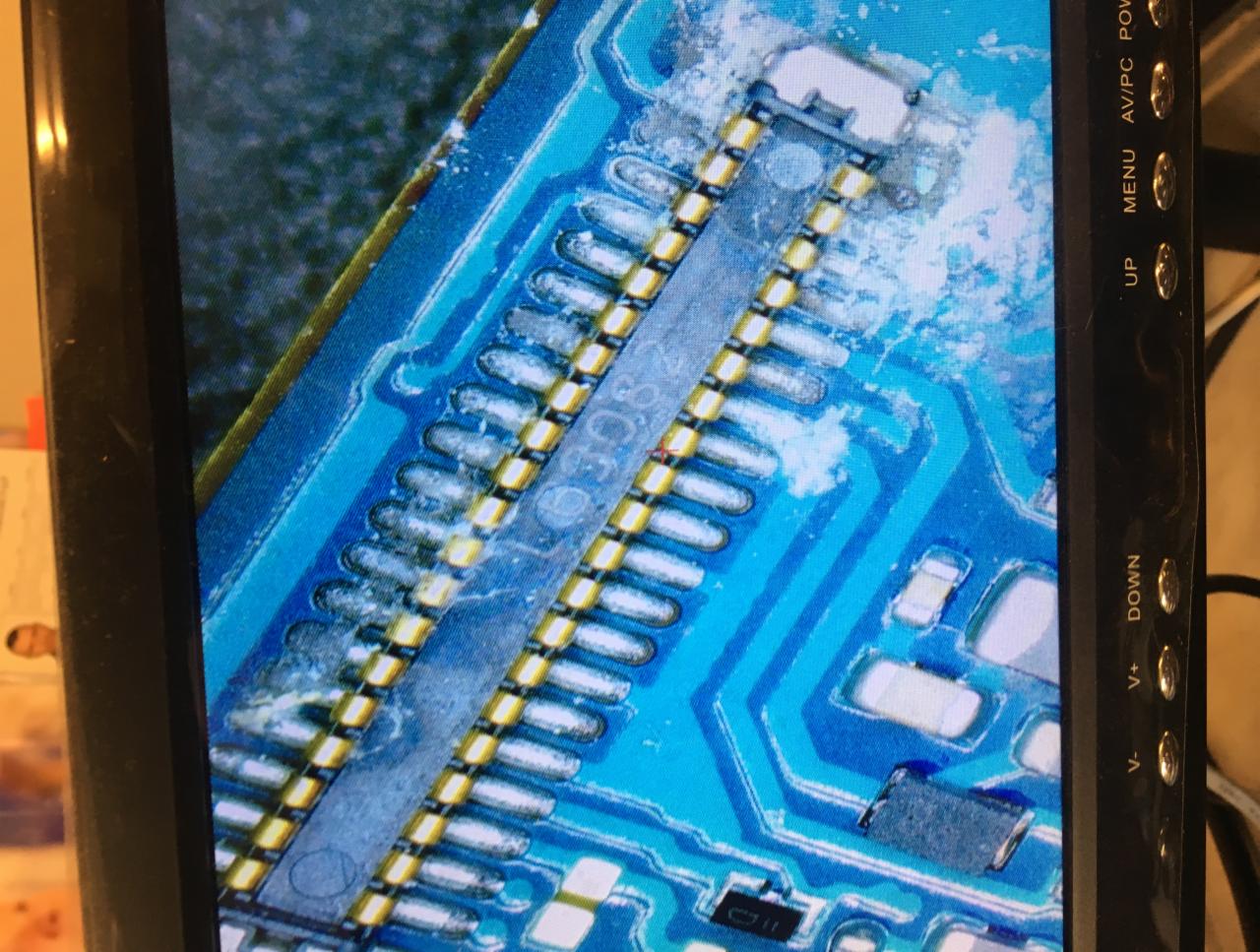 Zbliżenie na płytę główną telefonu pod mikroskopem, widoczne ślady lutowania i elementy elektroniczne.