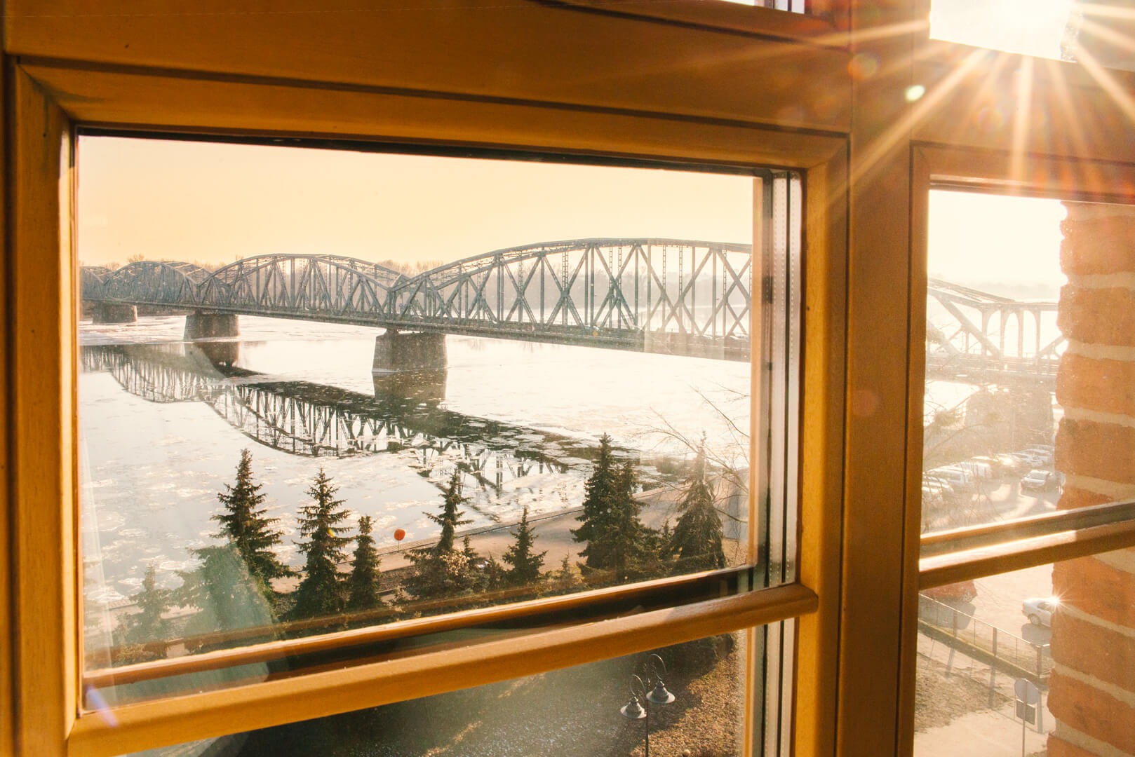 Widok z okna na most, rzekę z krą, drzewa i budynki w słoneczny dzień