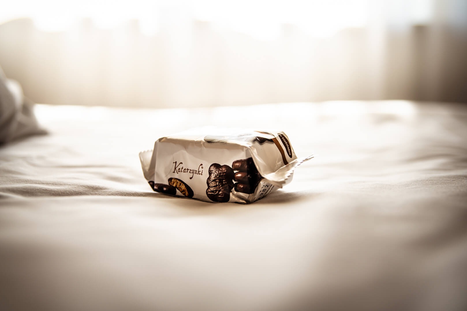 Otwarta paczka pierników w czekoladzie Katarzynki leży na białej pościeli w delikatnym świetle okiennym.