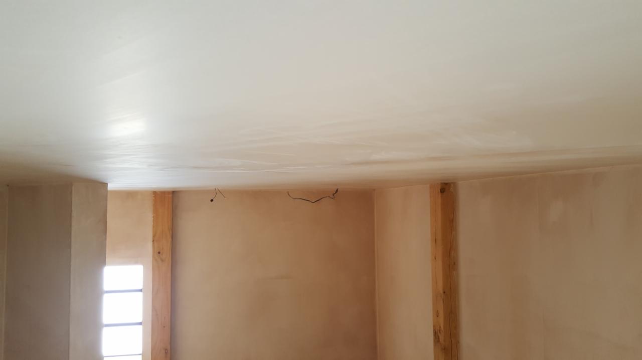 Świeżo nałożona gładź na suficie i ścianach w trakcie prac wykończeniowych, widoczne drewniane elementy konstrukcyjne i wystające przewody elektryczne.