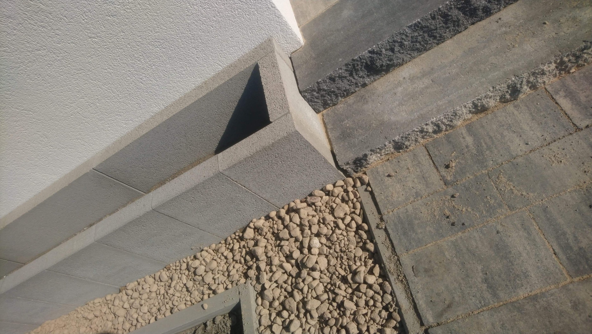 Szare płyty chodnikowe ułożone obok ściany budynku, z podsypką z drobnych kamieni, widoczne z góry, z bliska.